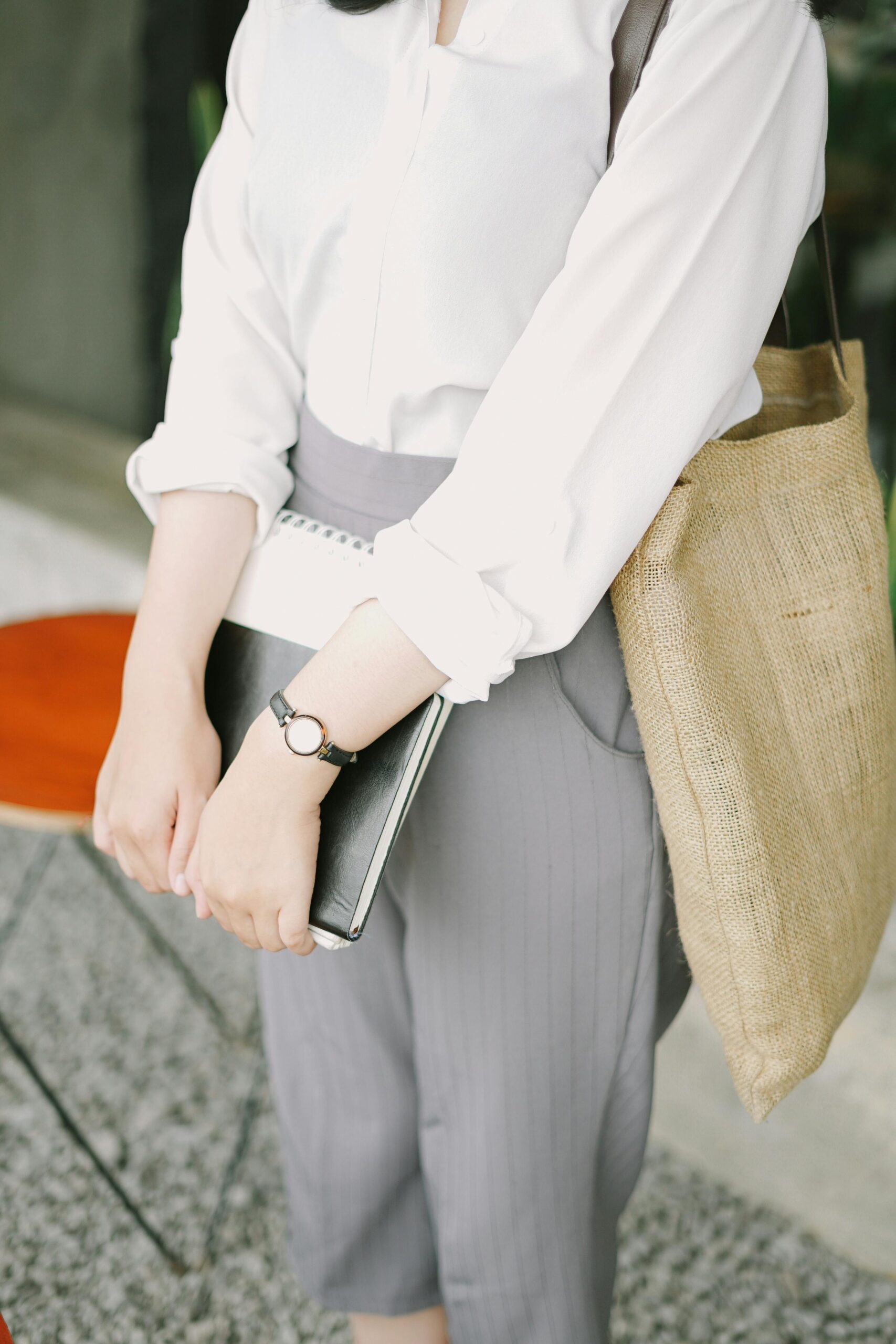 Woman in business attire holding a notebook with a jute bag in an office setting.